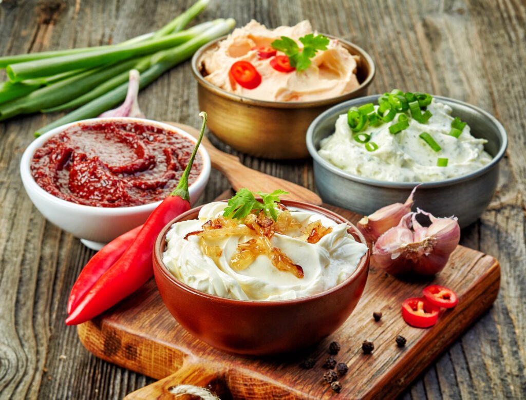 Four unbranded refrigerated dips arranged on a wooden board