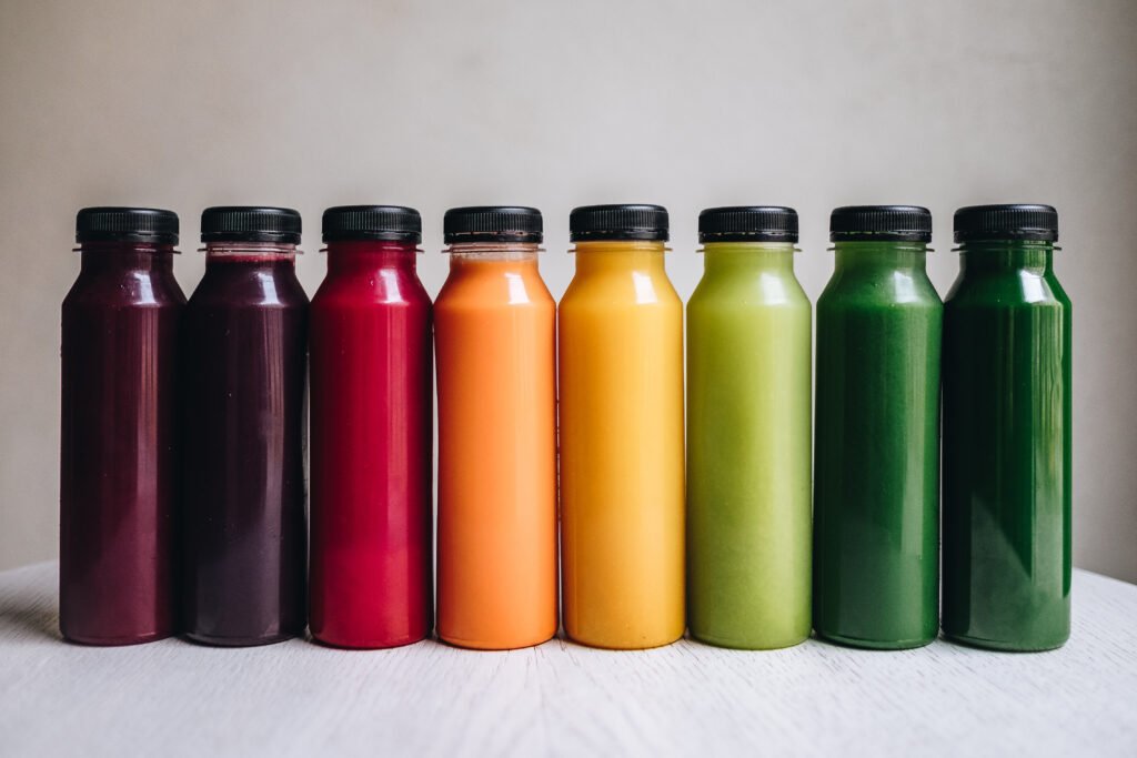 Eight unbranded cold-pressed juices in clear plastic bottles illustrating strong HPP packaging candidates
