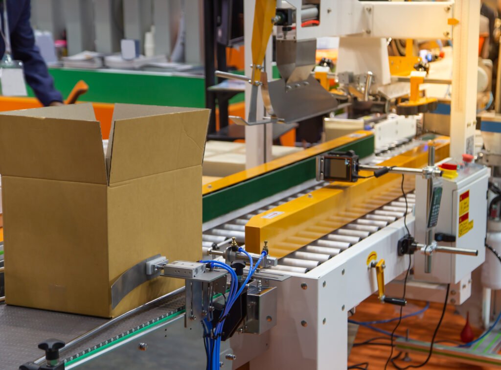 Open carton moving through automated conveyor equipment for post-HPP pack-off and assembly