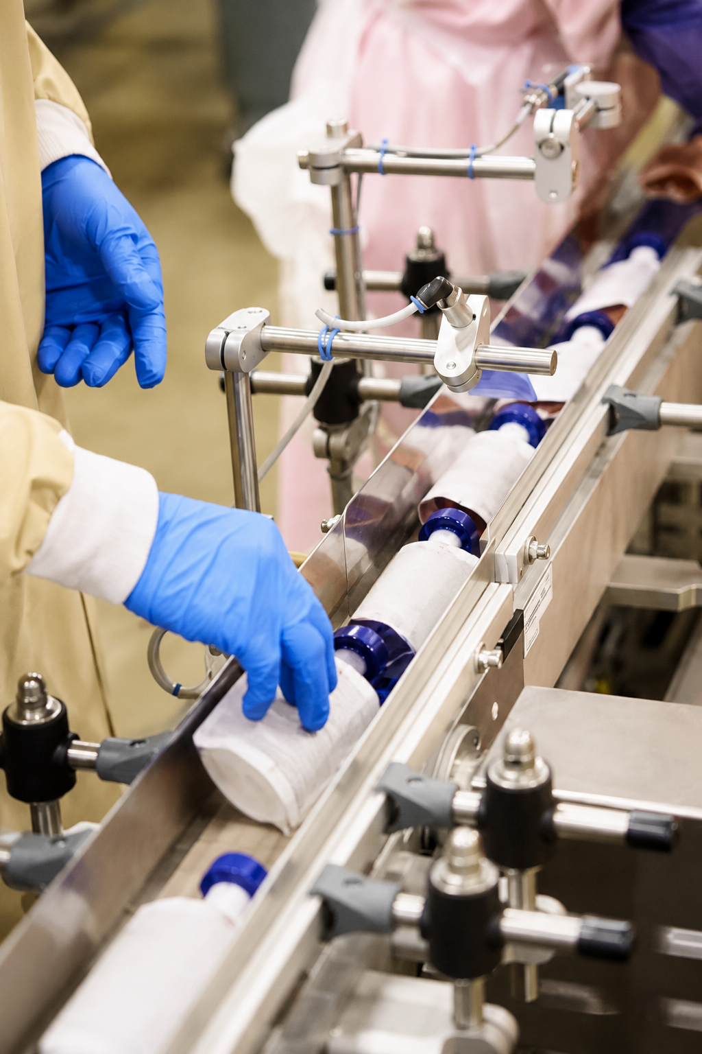Gloved worker handling unbranded squeeze pouches on an automated pouching line at an APC food manufacturing facility
