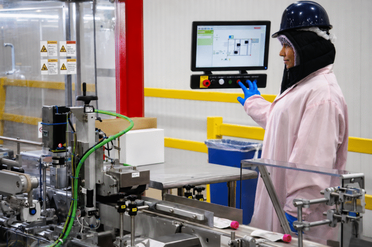 Worker operating a control panel beside an APC packaging line with unbranded white pouches