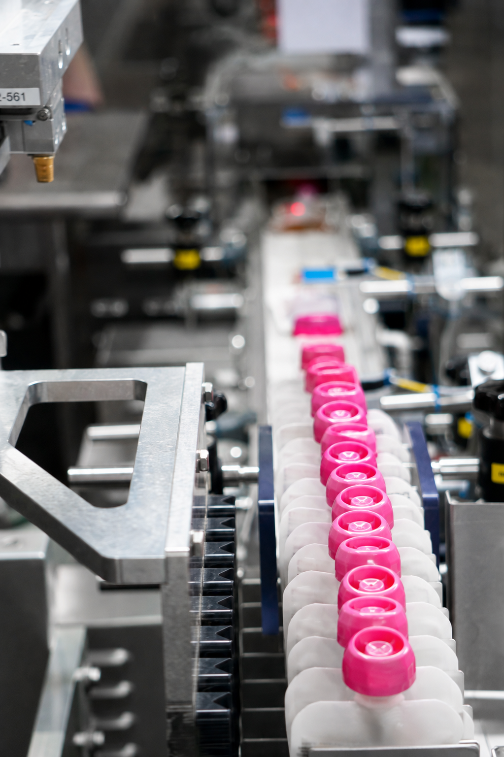Unbranded white flexible squeeze pouches with threaded pink caps moving through APC packaging equipment