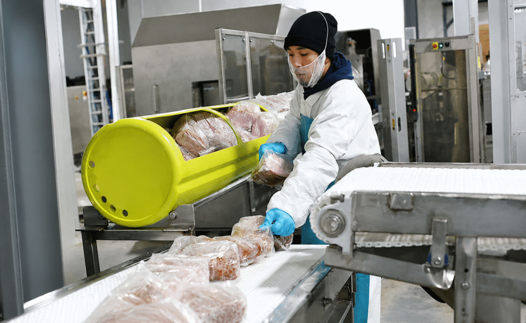 Worker loading vacuum-sealed protein packages into an HPP basket at APC