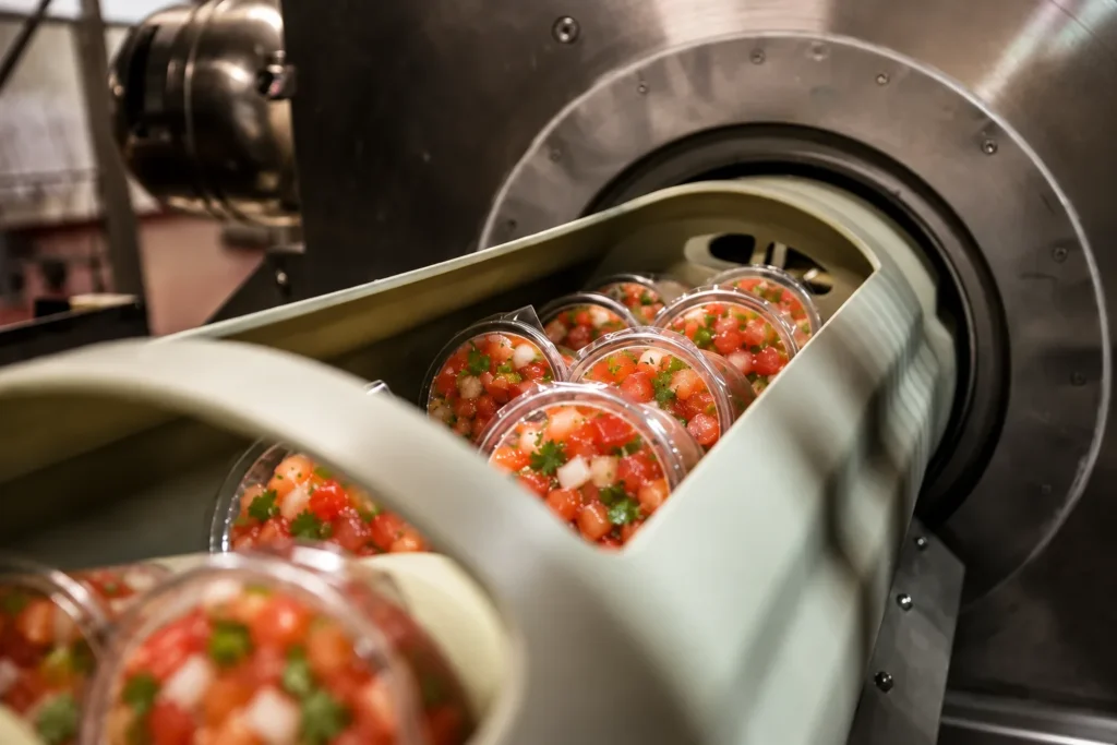 Chunky red pico de gallo cups in an HPP basket entering the high-pressure processing vessel at APC
