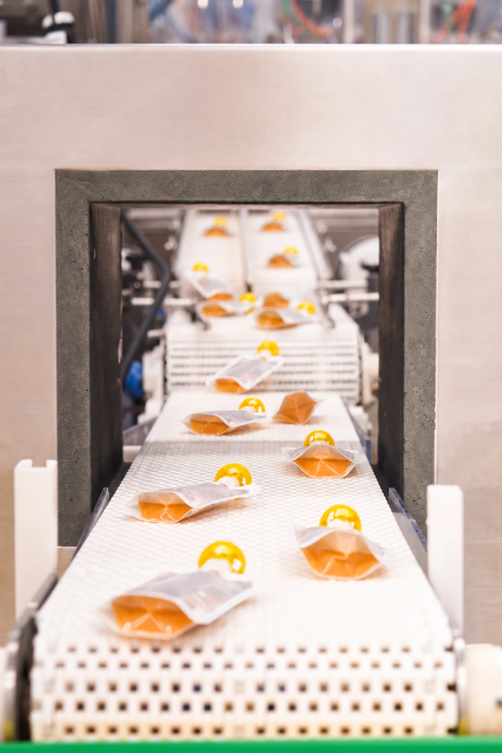 Clear flexible pouches with orange contents and yellow caps moving along a white processing conveyor.