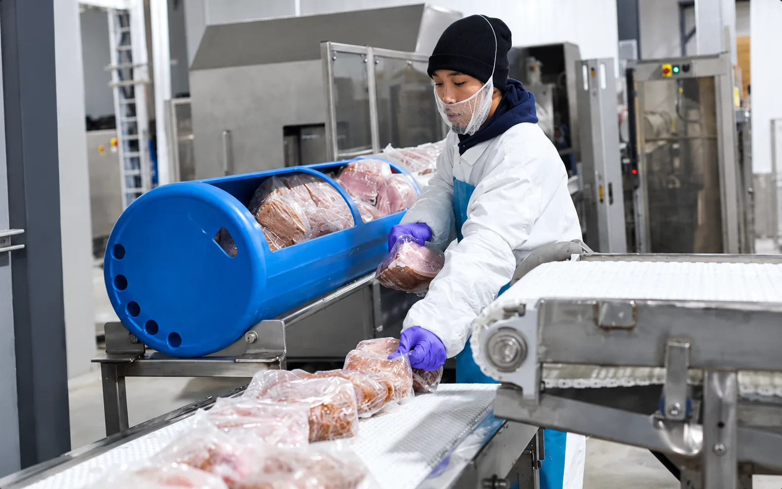 Worker wearing purple gloves loading vacuum-sealed protein packages into a blue HPP basket at APC