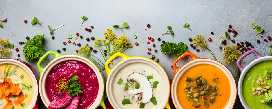 Assorted colorful sauces and purees in bowls with herbs and vegetables.