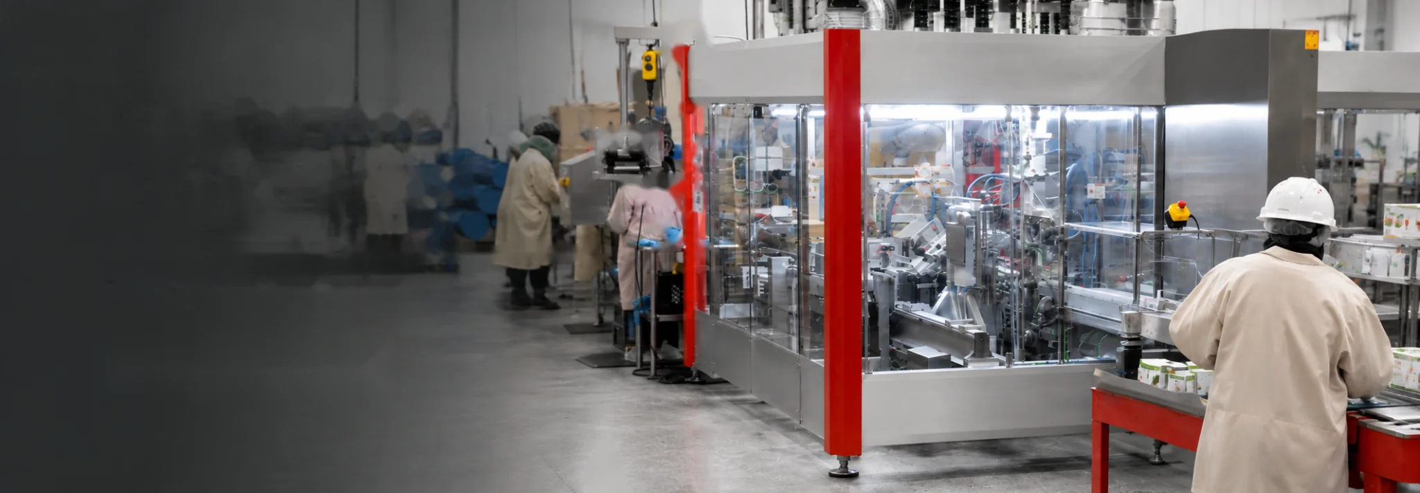 Wide view of an APC food manufacturing floor with red-framed packaging equipment and employees working along the production line.